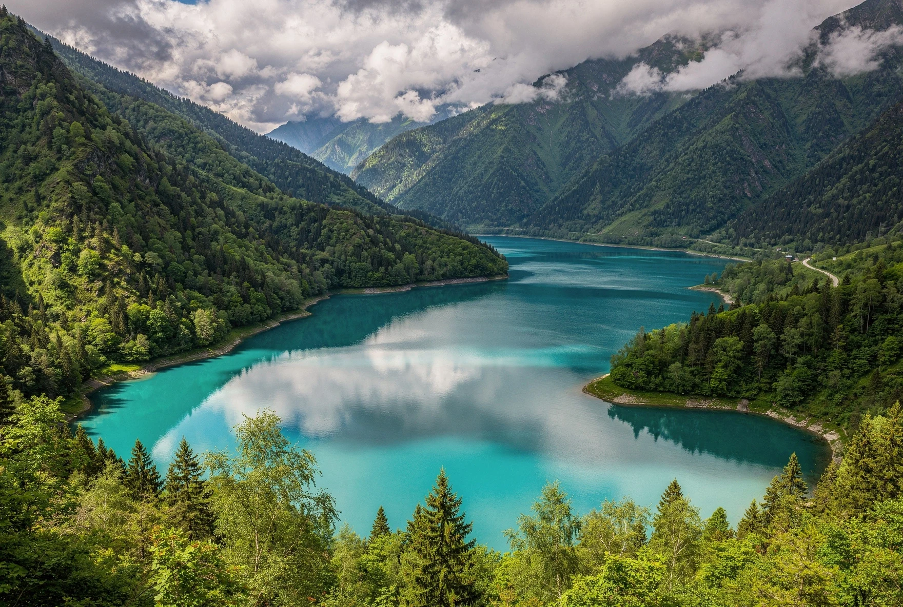 Turquoise Jinvali Reservoir surrounded by lush green forested mountains in the Caucasus