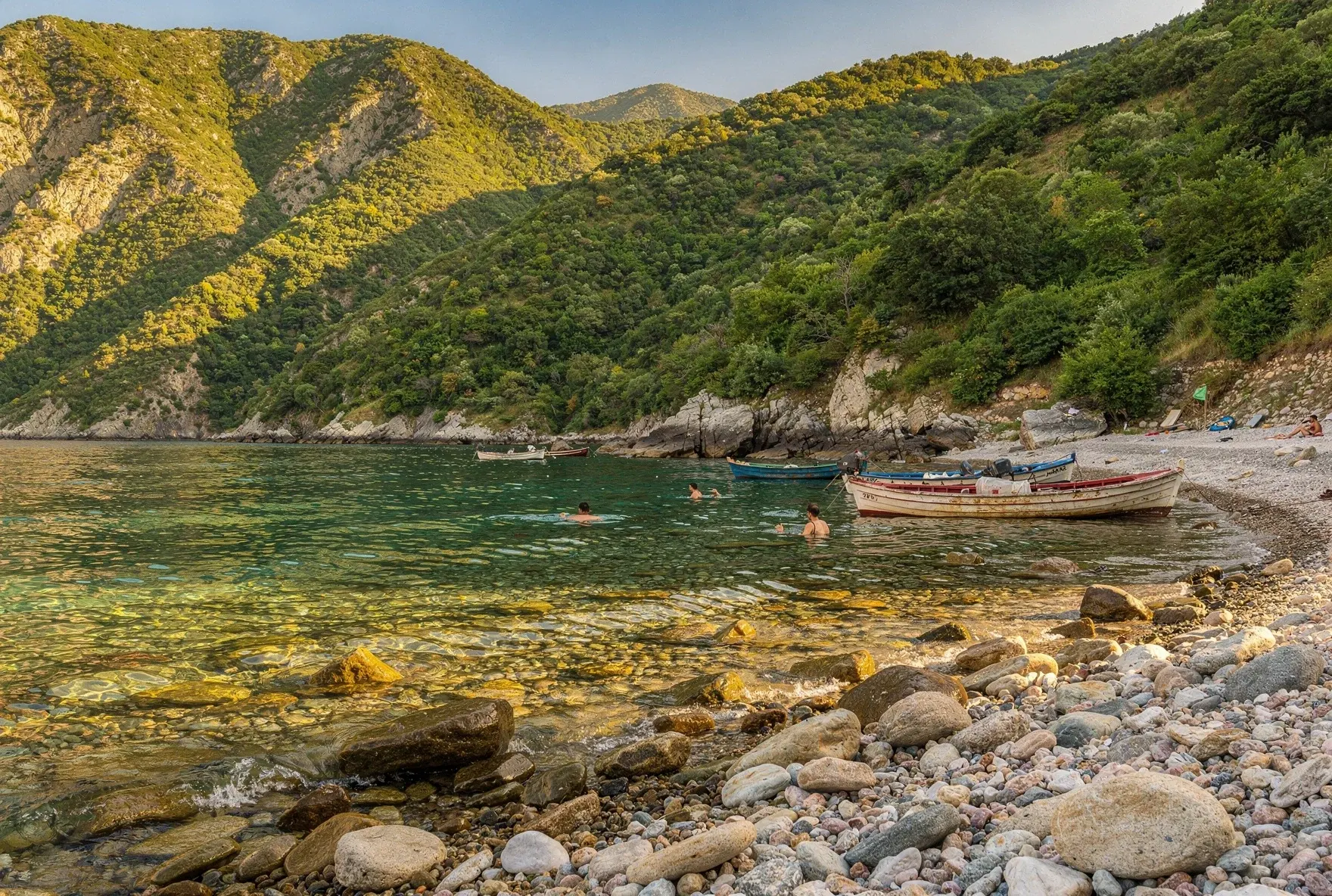 Clear turquoise water at a pebbly beach cove along Georgia's Black Sea coast with green mountains rising from the shore