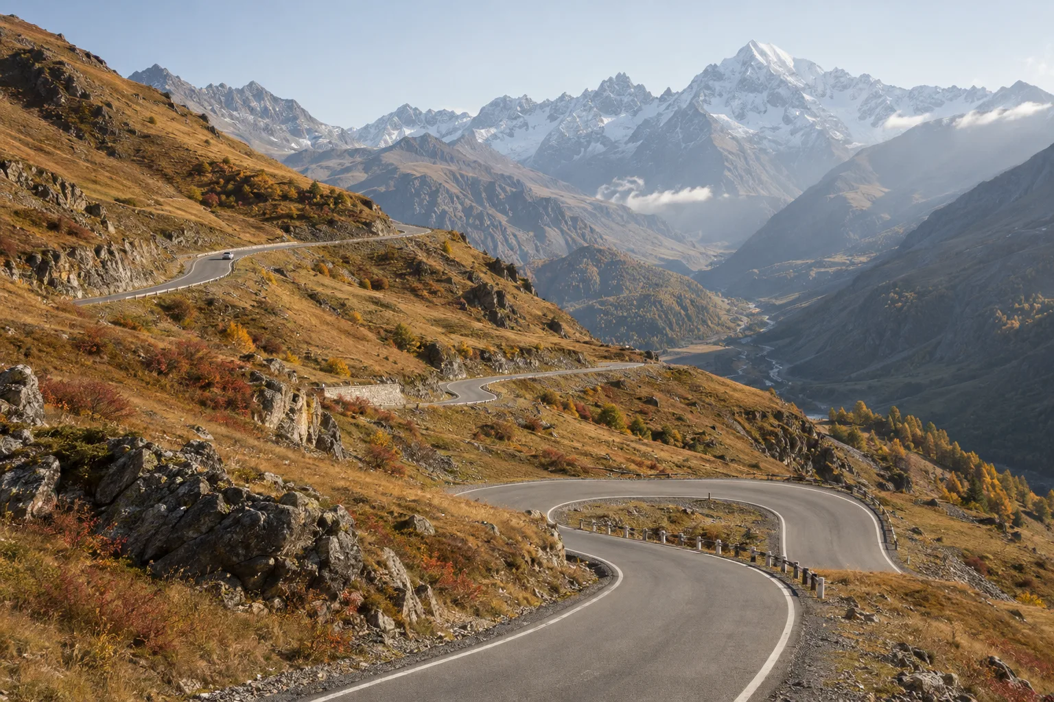 A sealed two-lane road climbing in switchbacks towards a high pass in the Greater Caucasus with autumn colour on the slopes