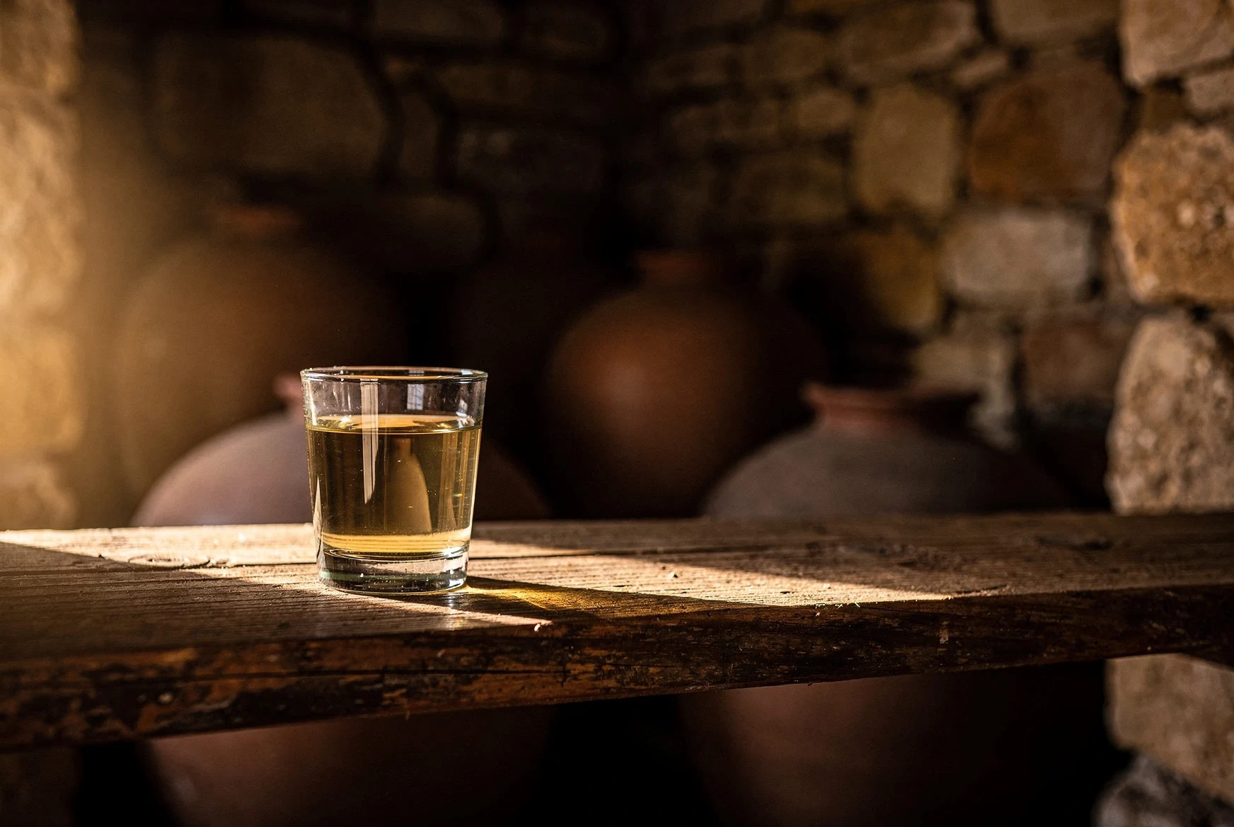 Small glass of spirit on a wooden shelf in a dim cellar
