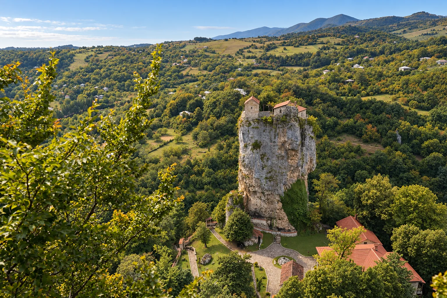 Katskhi Pillar, a 40-metre limestone column with a small stone church on its flat top, rising out of wooded hills in Imereti with the monastery buildings at its base