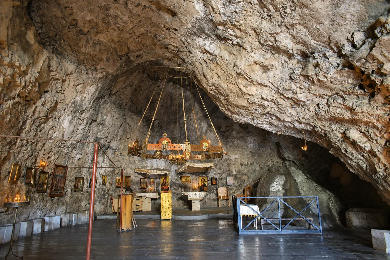 Inside the cave church at Mgvimevi convent near Chiatura, a brass chandelier hanging from the rock ceiling above icons, candles and a low wooden rail