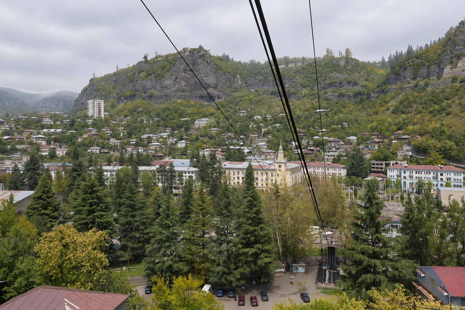 Chiatura seen from a cable car cabin, the cables running down over the trees to the yellow town hall tower with the cliffs of the Qvirila gorge behind