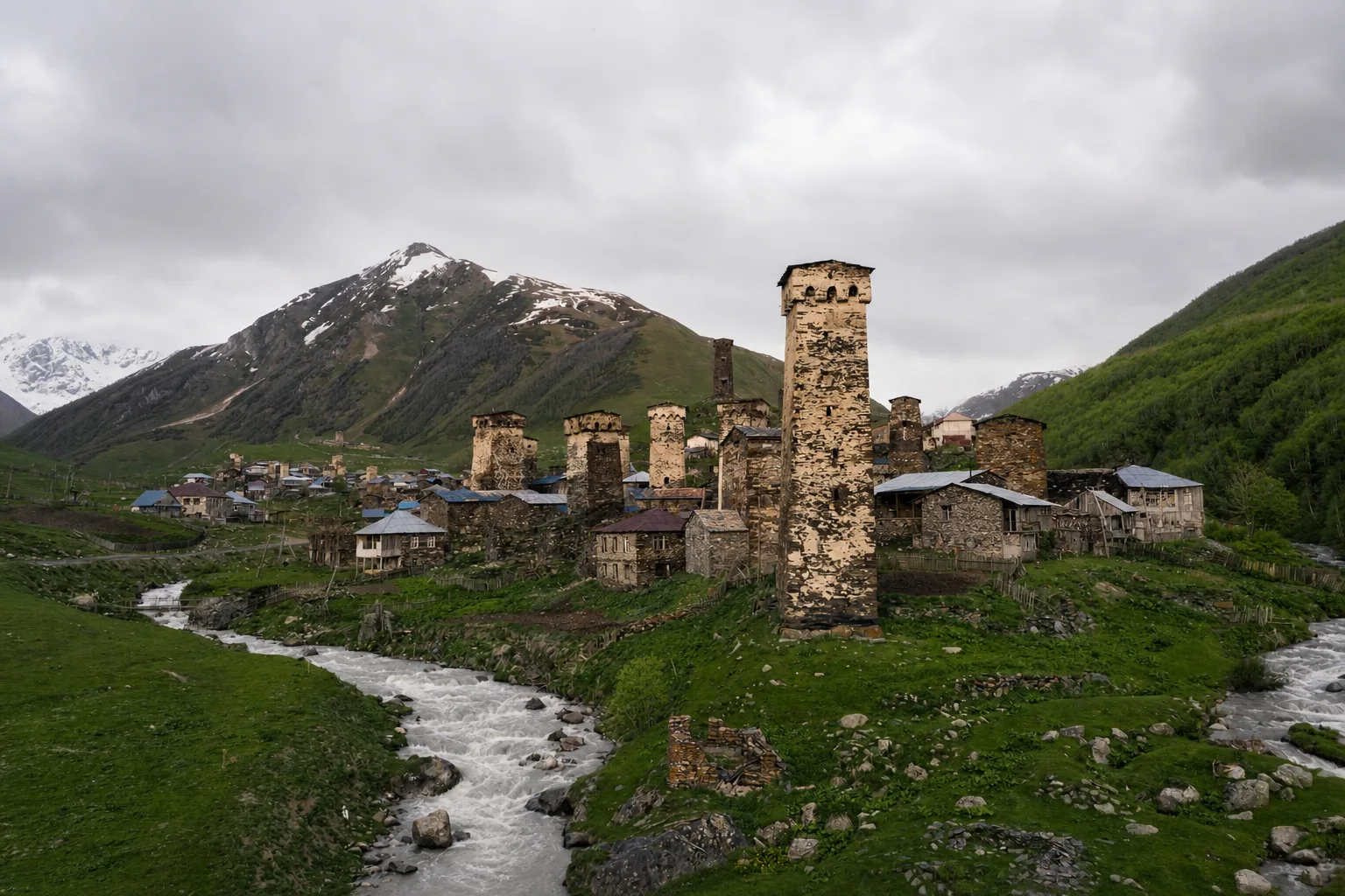 A stone Svan tower with a slate roof among low houses in Ushguli on an overcast autumn afternoon
