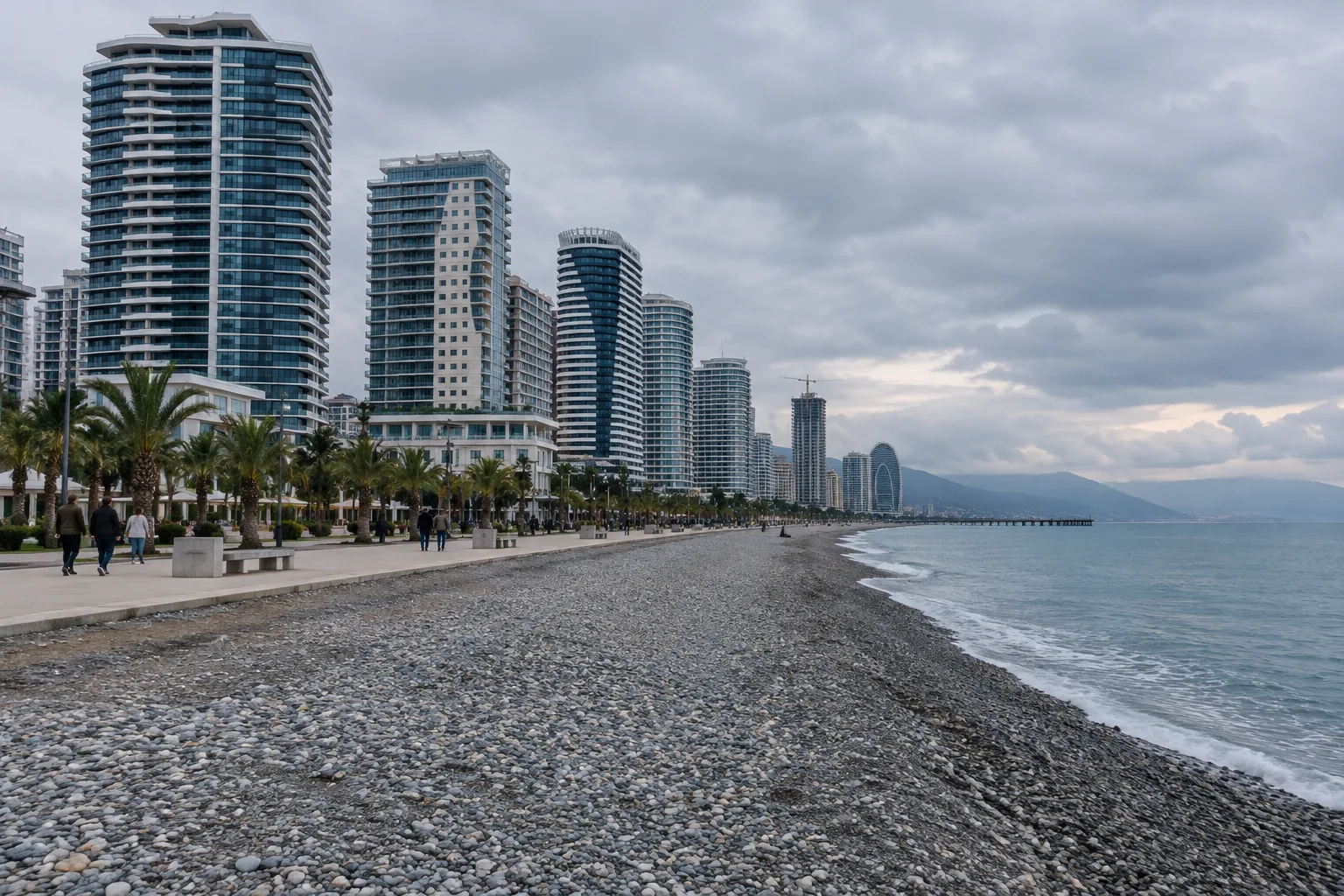 Row of tall new apartment towers along the wide seafront promenade of Batumi's new boulevard with the pebble beach in front on an overcast afternoon