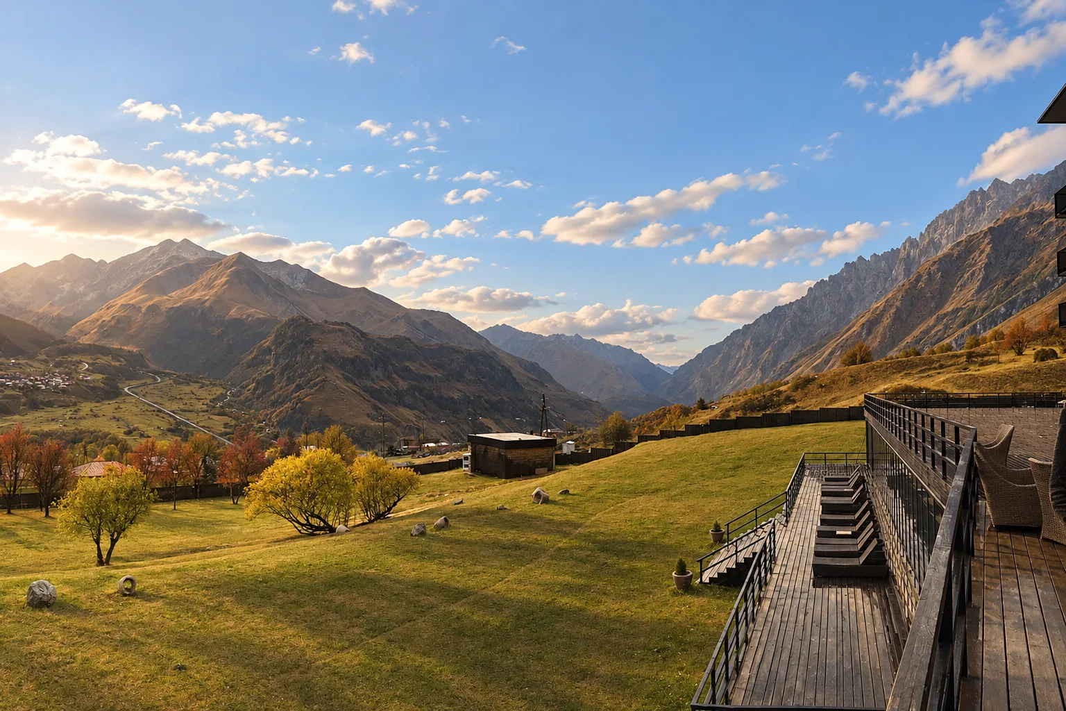 Wooden terrace and lawn of Rooms Hotel Kazbegi facing the mountains across the valley on an autumn afternoon