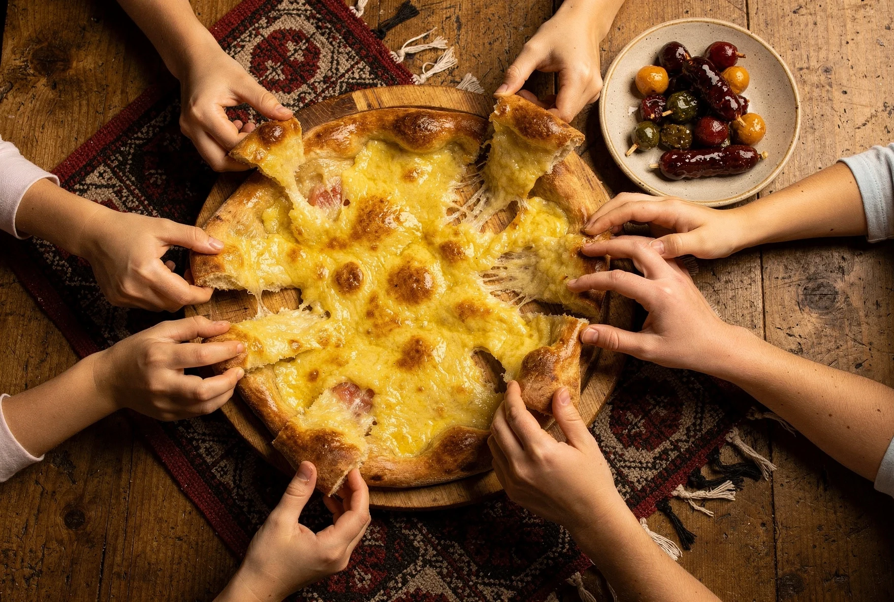 Family hands reaching for khachapuri cheese bread at a Georgian restaurant
