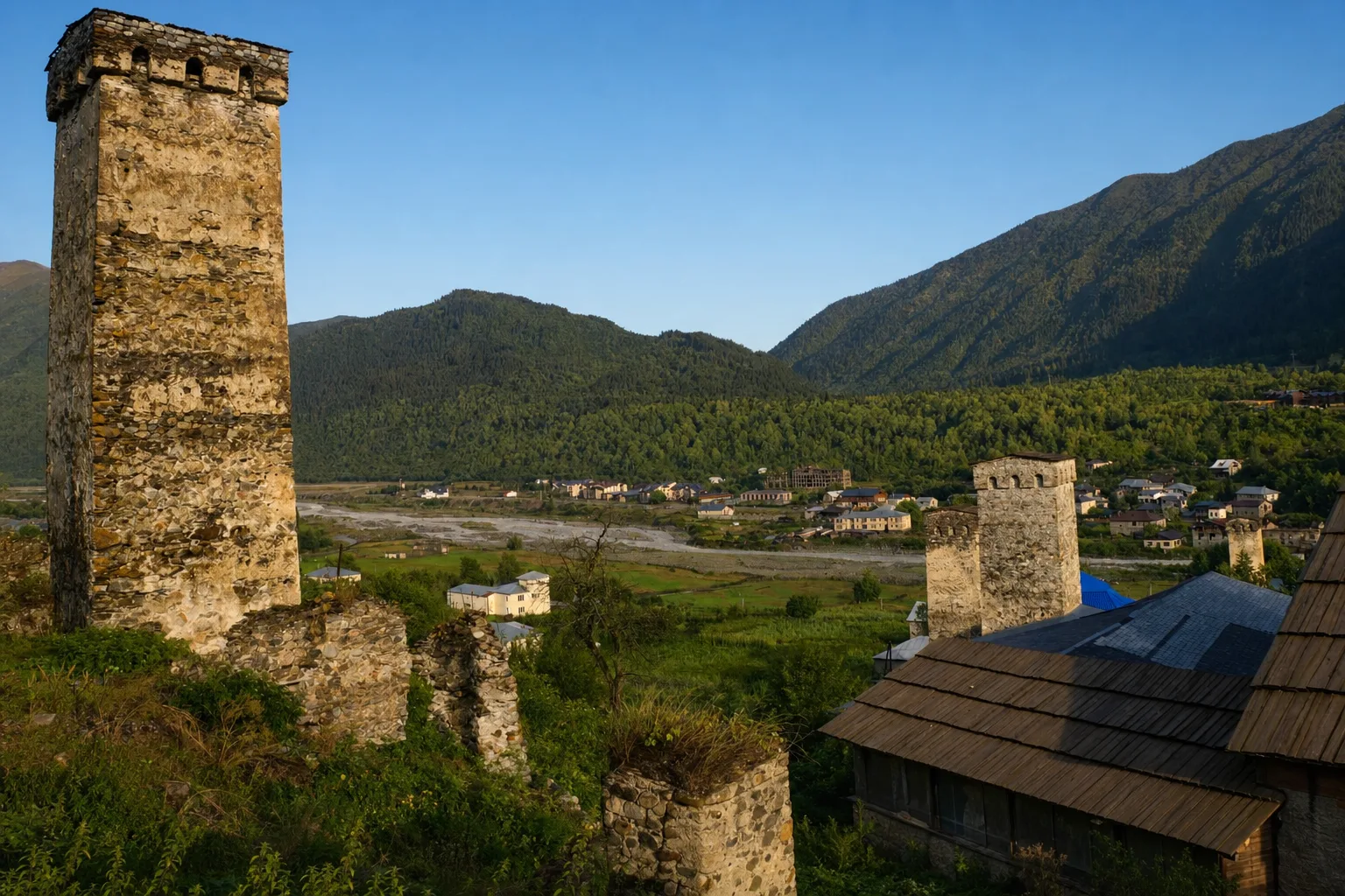 Stone defensive towers and slate-roofed houses of Mestia in Svaneti in low afternoon light, with the Mulkhura valley and forested mountains behind