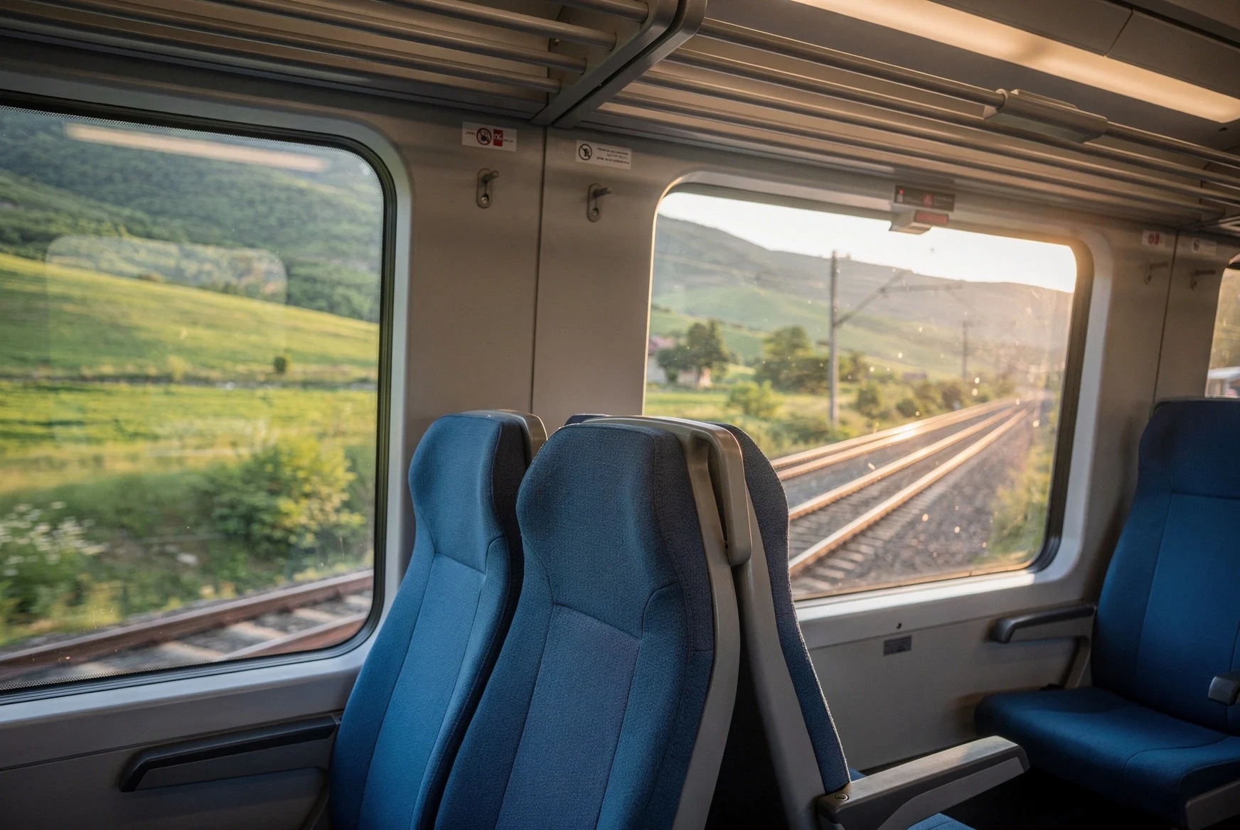 View from inside a passenger train in Georgia looking out at green hills and electrified tracks