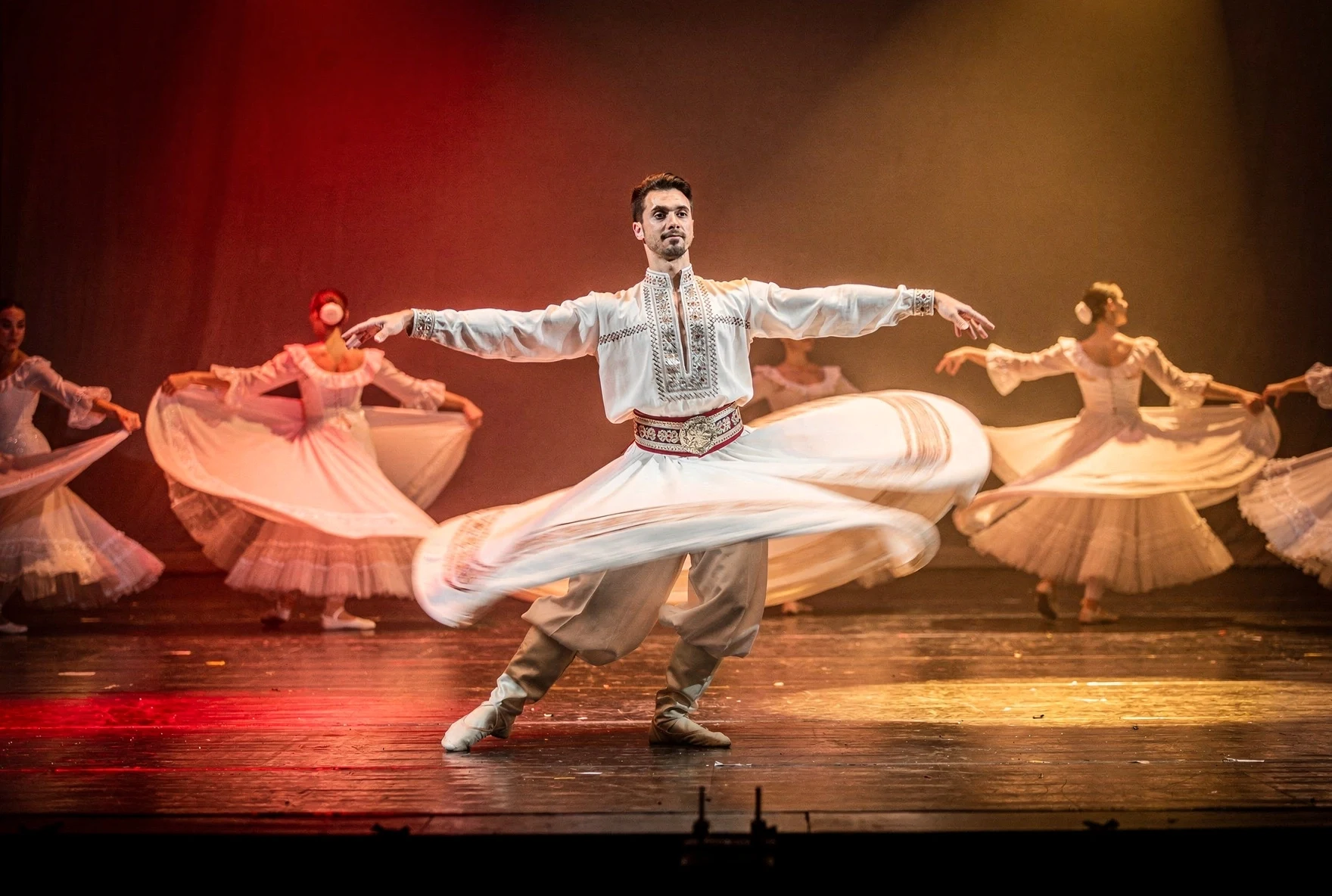 Georgian national ballet dancer spinning on stage in traditional white chokha costume with dramatic red and amber lighting