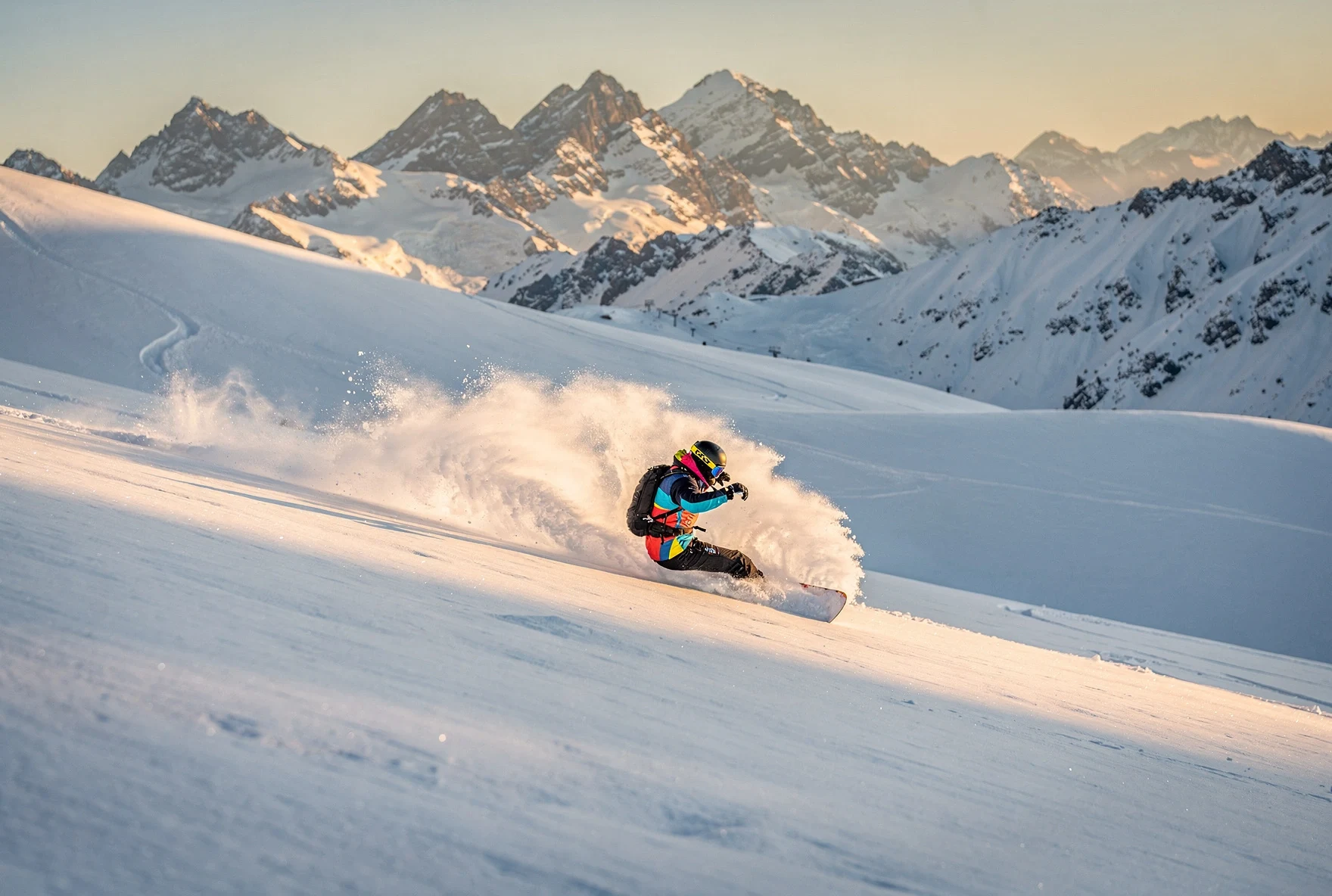 Snowboarder carving through deep powder on off-piste terrain at Gudauri with the Caucasus mountains in the background
