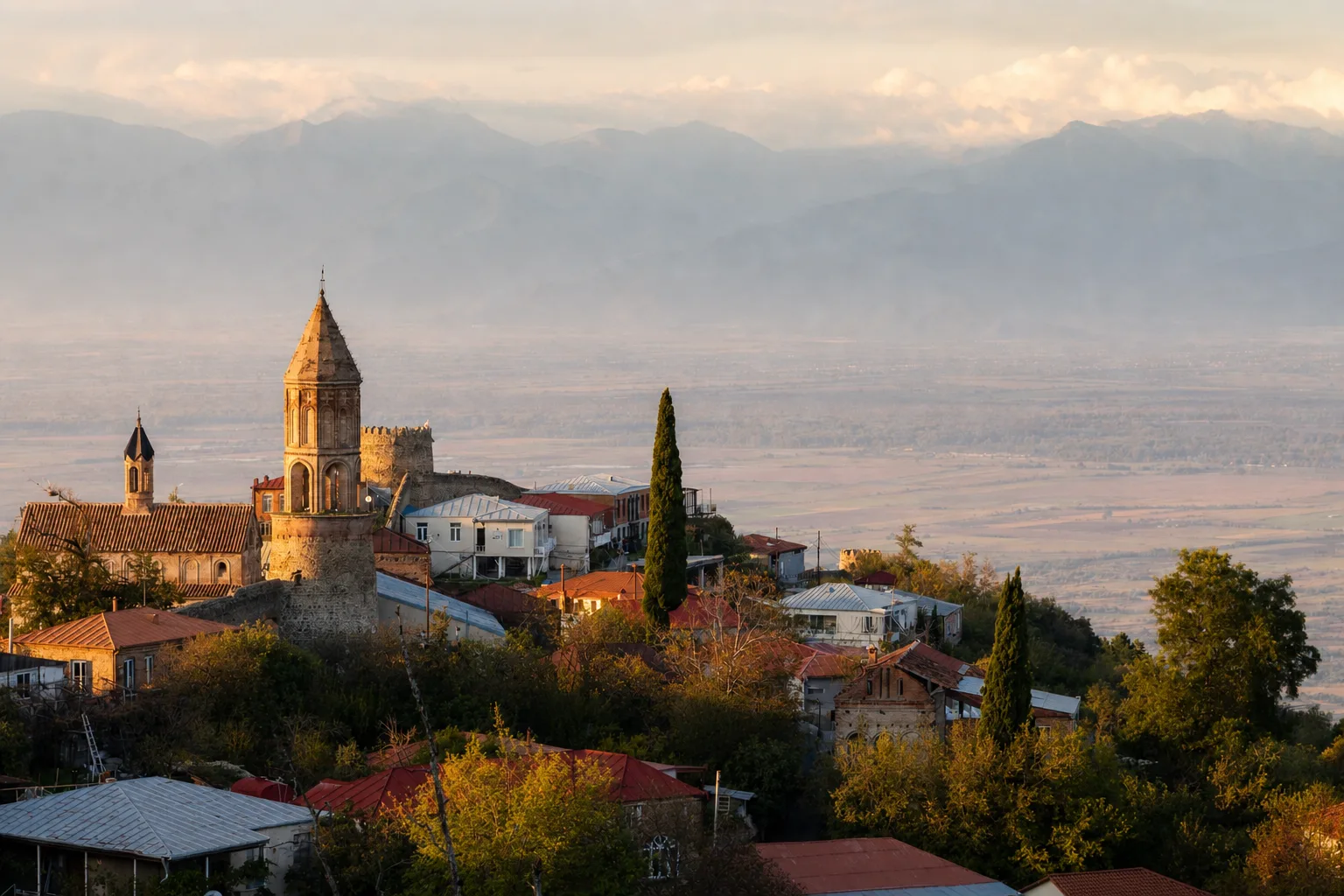 Sighnaghi's church tower, tiled roofs and town wall on the hillside above the hazy Alazani valley in late afternoon light
