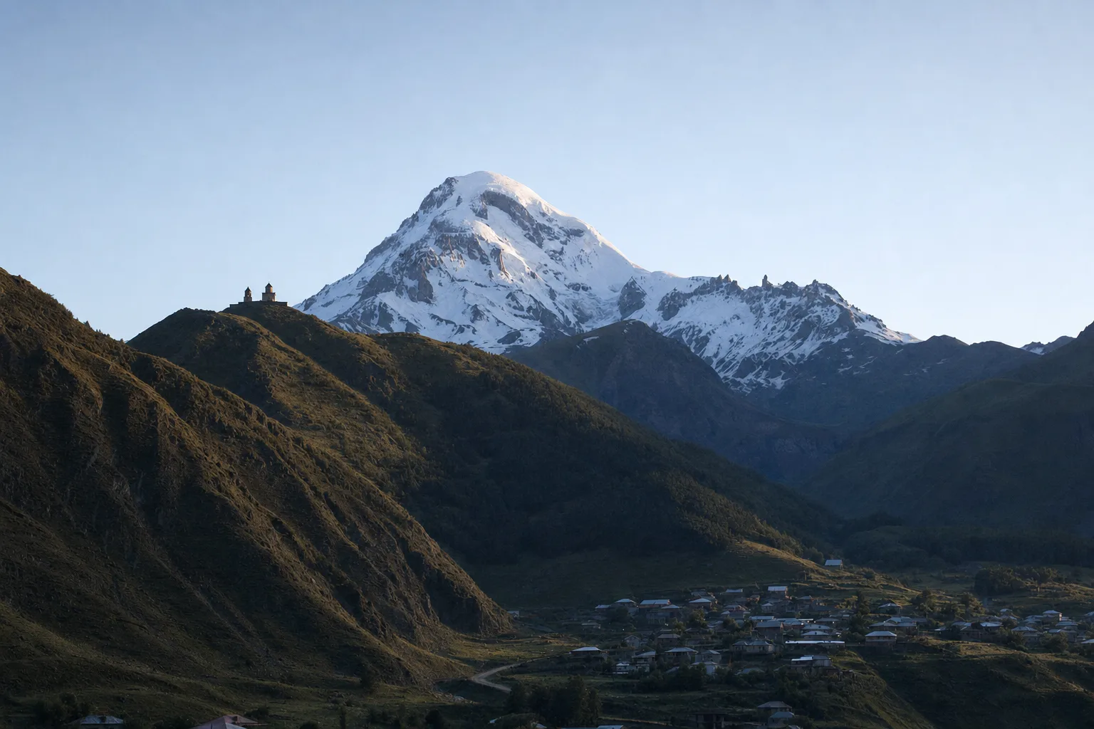 Gergeti Trinity Church on its grassy ridge above Stepantsminda with the snow-capped summit of Mount Kazbek behind