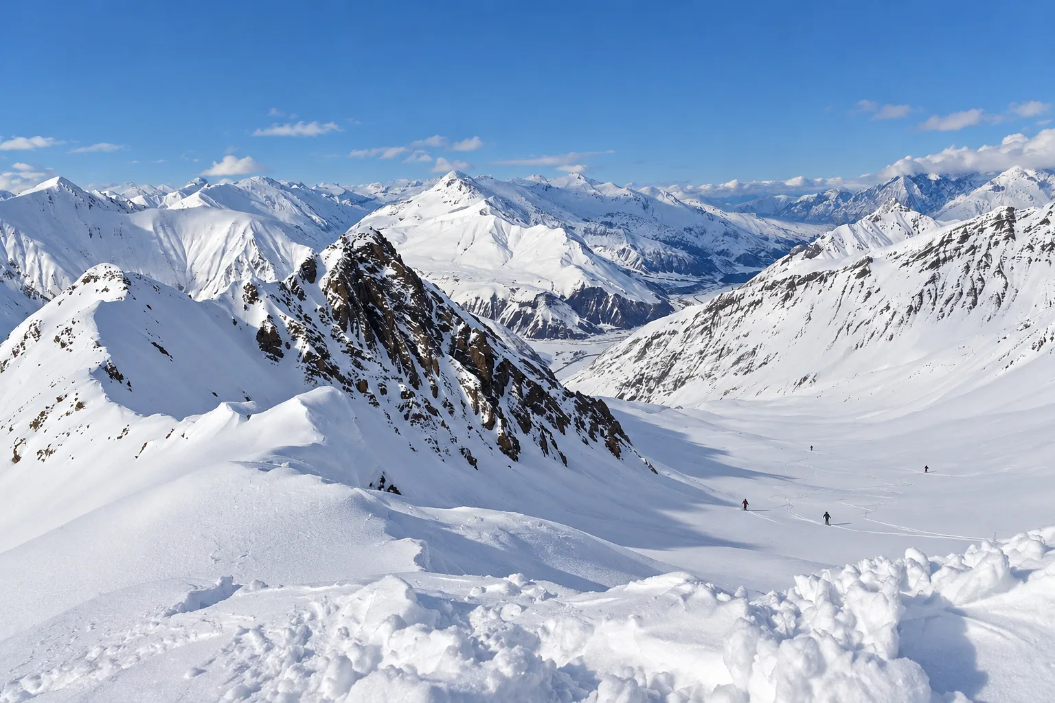 Deep settled snow on the open bowls and ridges above Gudauri in mid-January under a clear sky, with a few distant skiers and the Greater Caucasus behind
