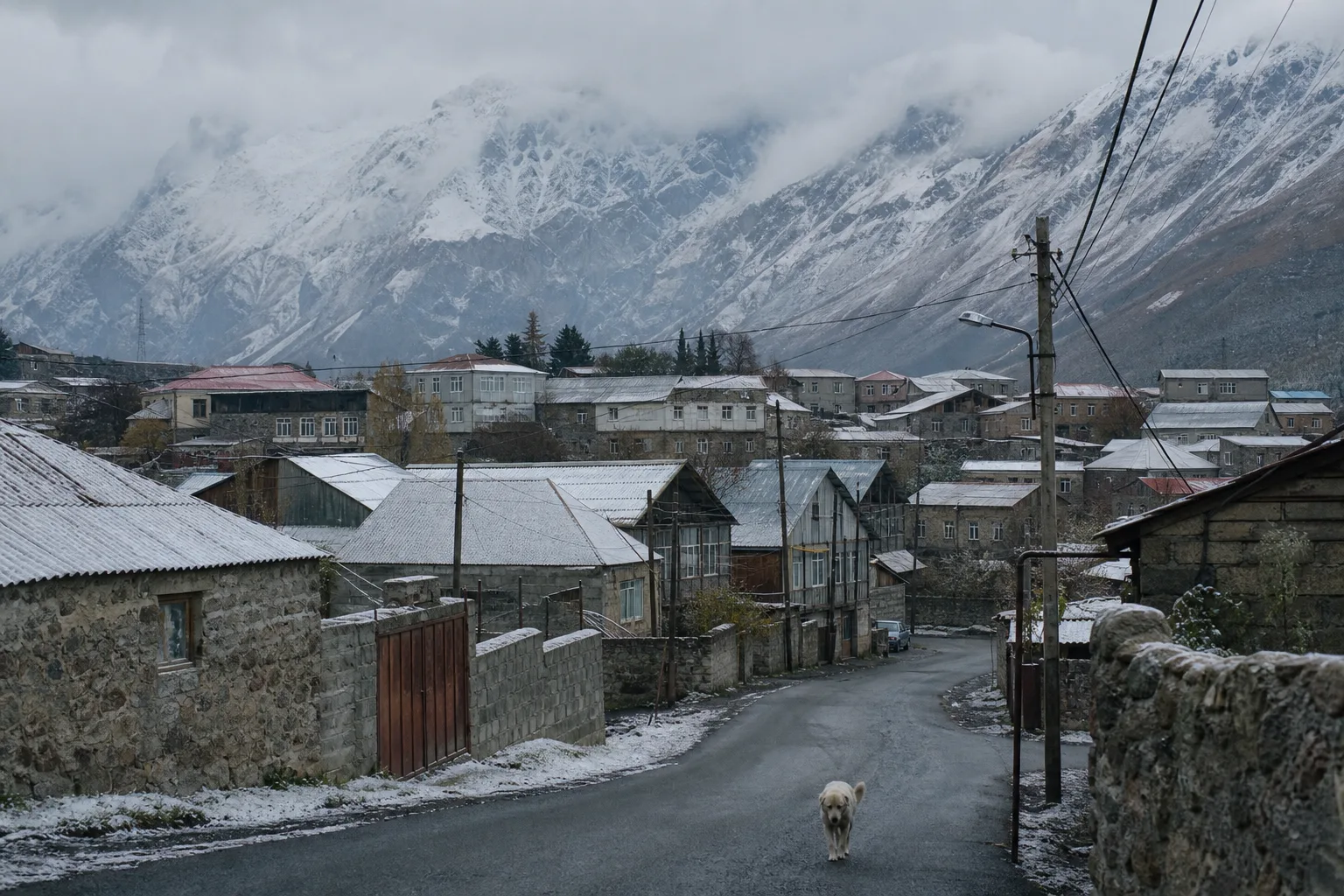 Stone and tin-roofed houses of Stepantsminda under a first light snow with the Caucasus behind in cloud