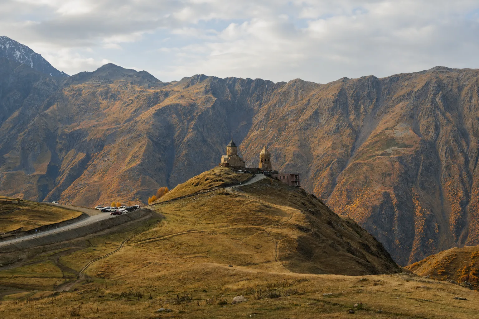 Gergeti Trinity Church on its ridge in autumn with the Caucasus wall behind
