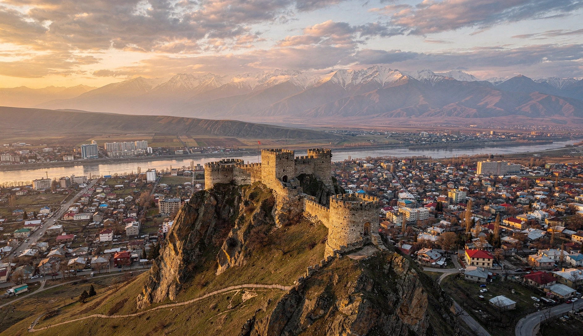 Gori Fortress perched on a rocky hill overlooking the city at golden hour with Caucasus mountains in the background