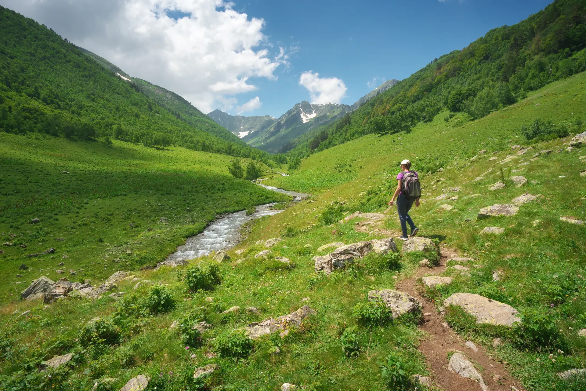 Solo hiker walking along a mountain trail beside a stream in a green alpine valley in Georgia