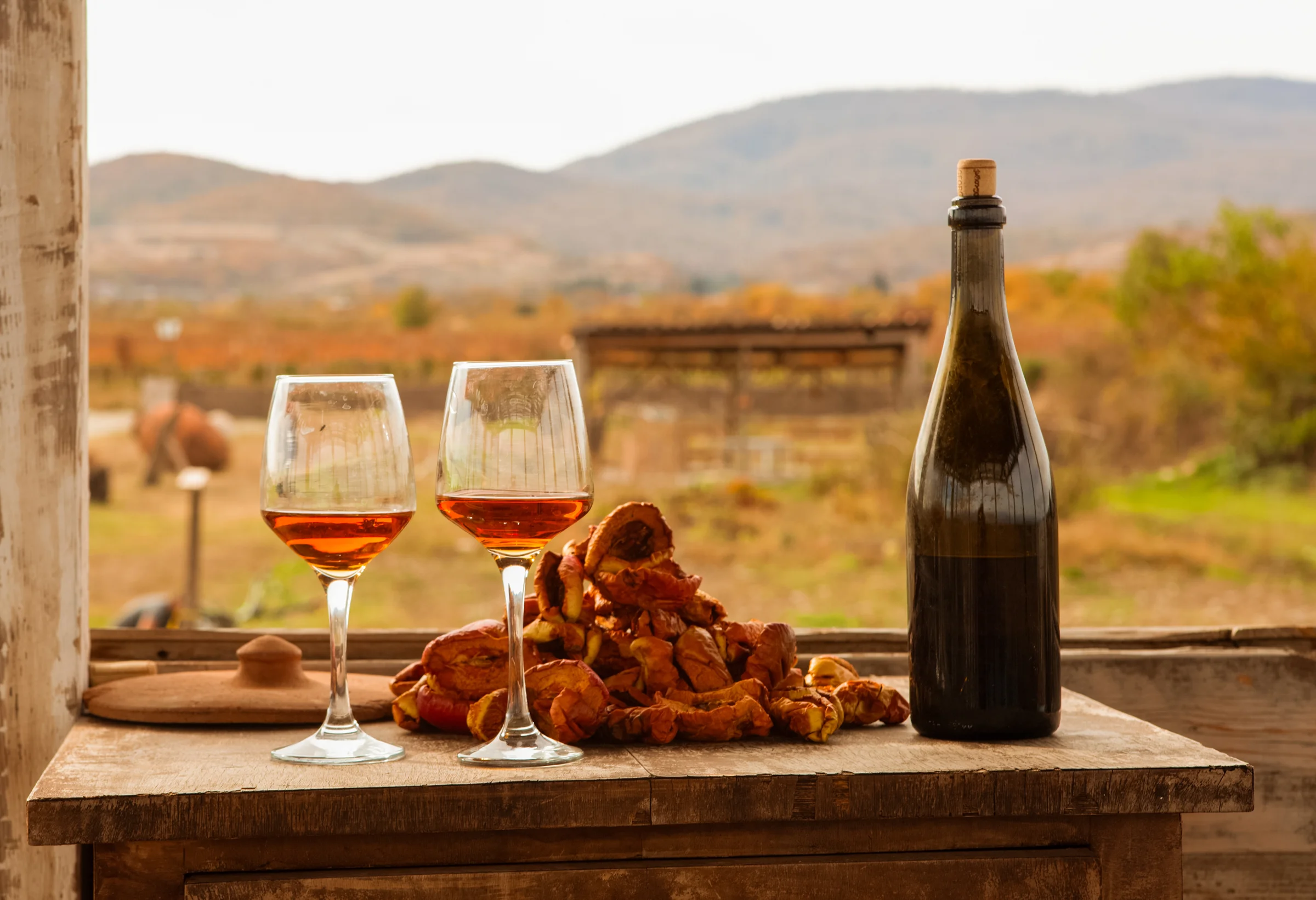 Amber wine glasses and bottle on a rustic table overlooking Georgian countryside