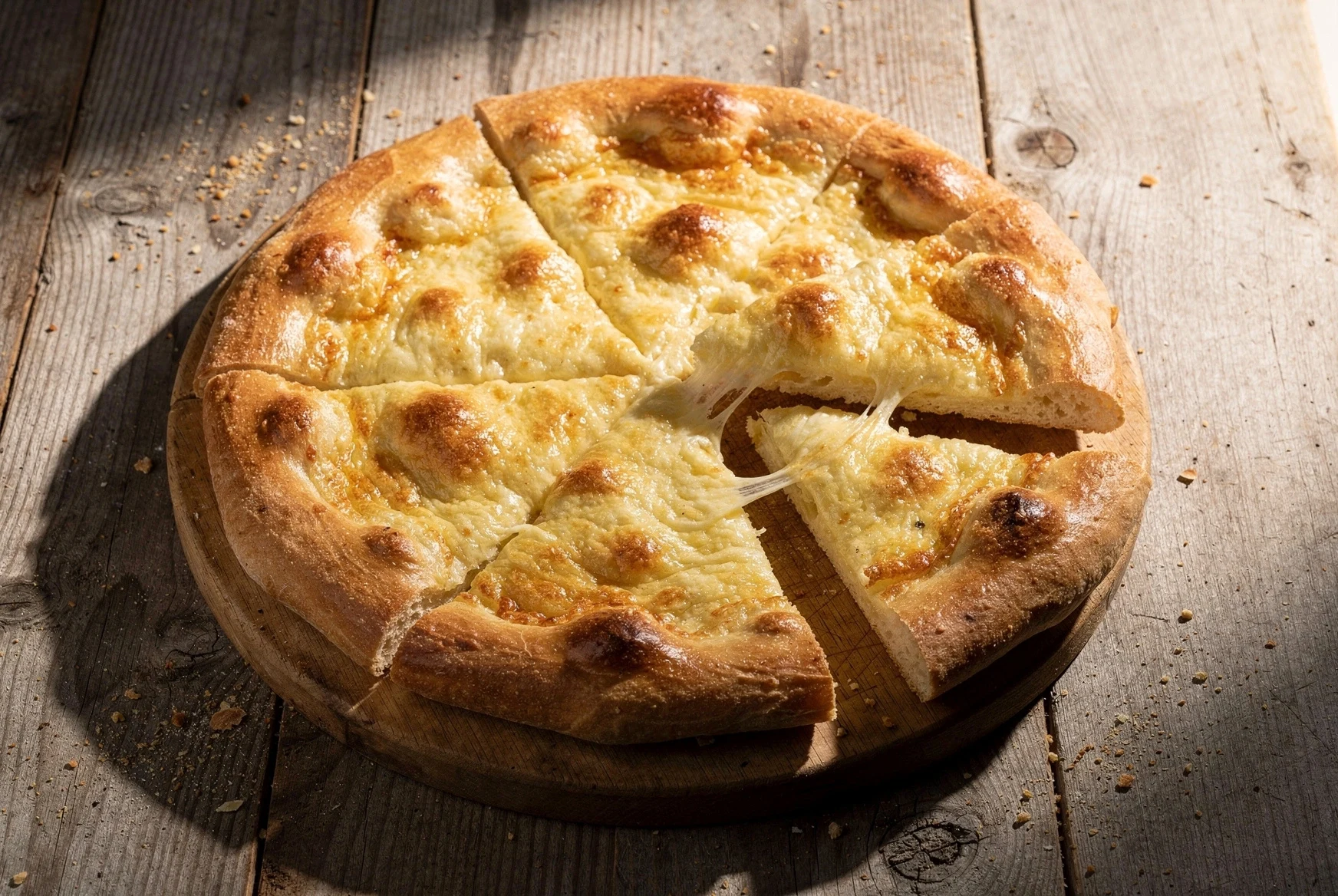 Round Imeruli khachapuri sliced on a wooden board with melted cheese visible