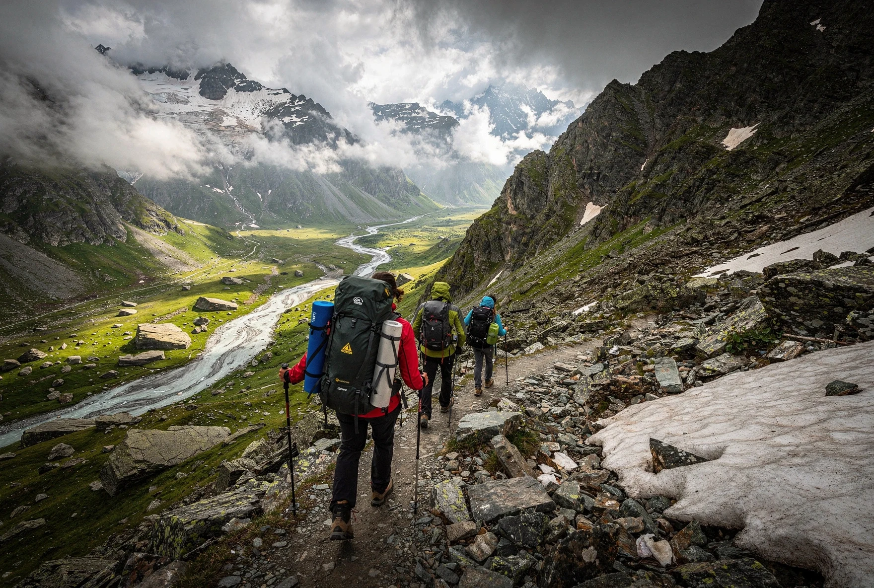 Hikers crossing a high mountain pass in the Caucasus with dramatic views of a glacial valley below