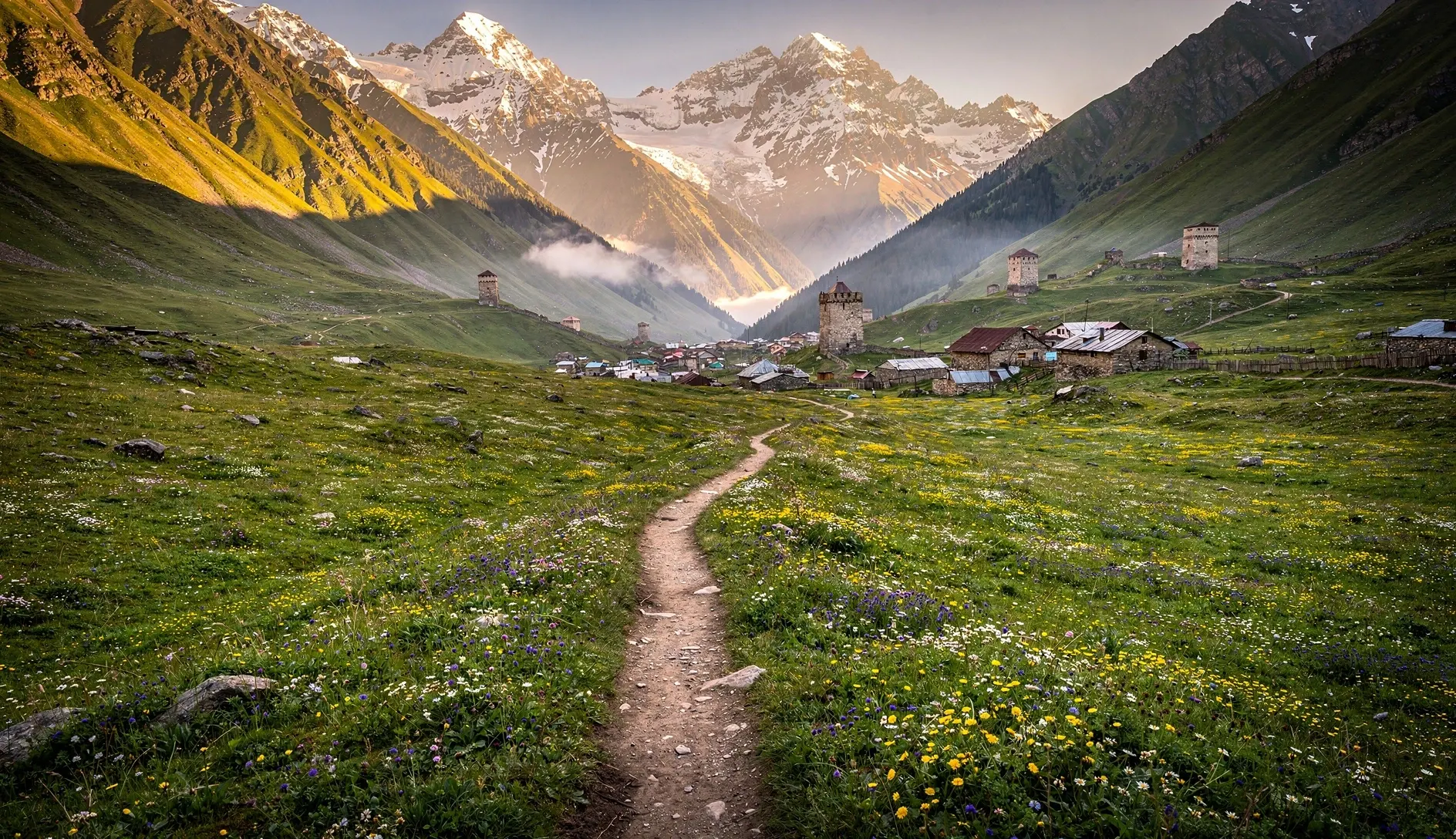 Hiking trail winding through an alpine valley in Svaneti, Georgia, with medieval stone towers and snow-capped Caucasus peaks in the background
