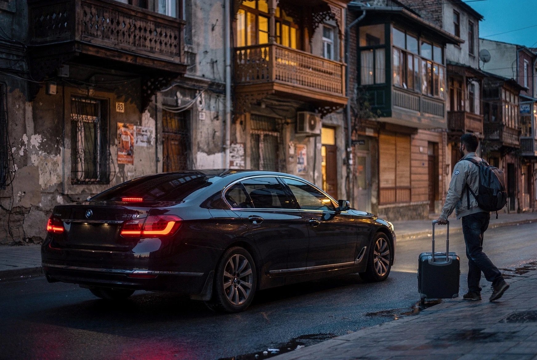Traveler approaching a waiting car on an old Tbilisi street at dusk