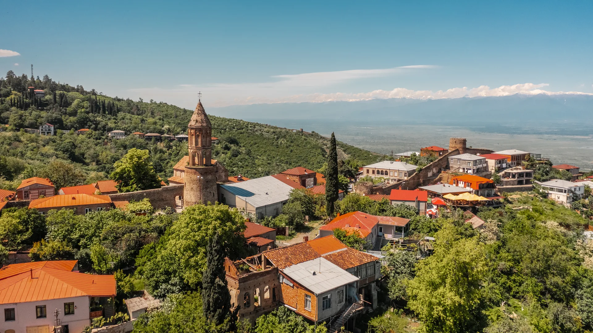 Panoramic view of Sighnaghi with its red rooftops, church bell tower, and fortress tower, the Alazani Valley and Caucasus Mountains in the background