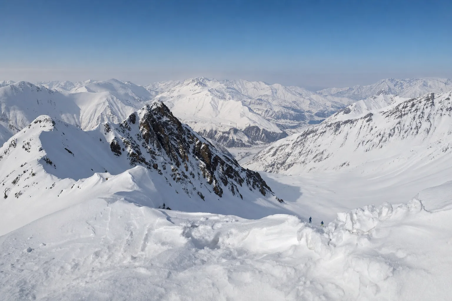 Snow-covered ridges of the Greater Caucasus seen from the top lift at Gudauri on a clear winter morning, with two skiers in the distance