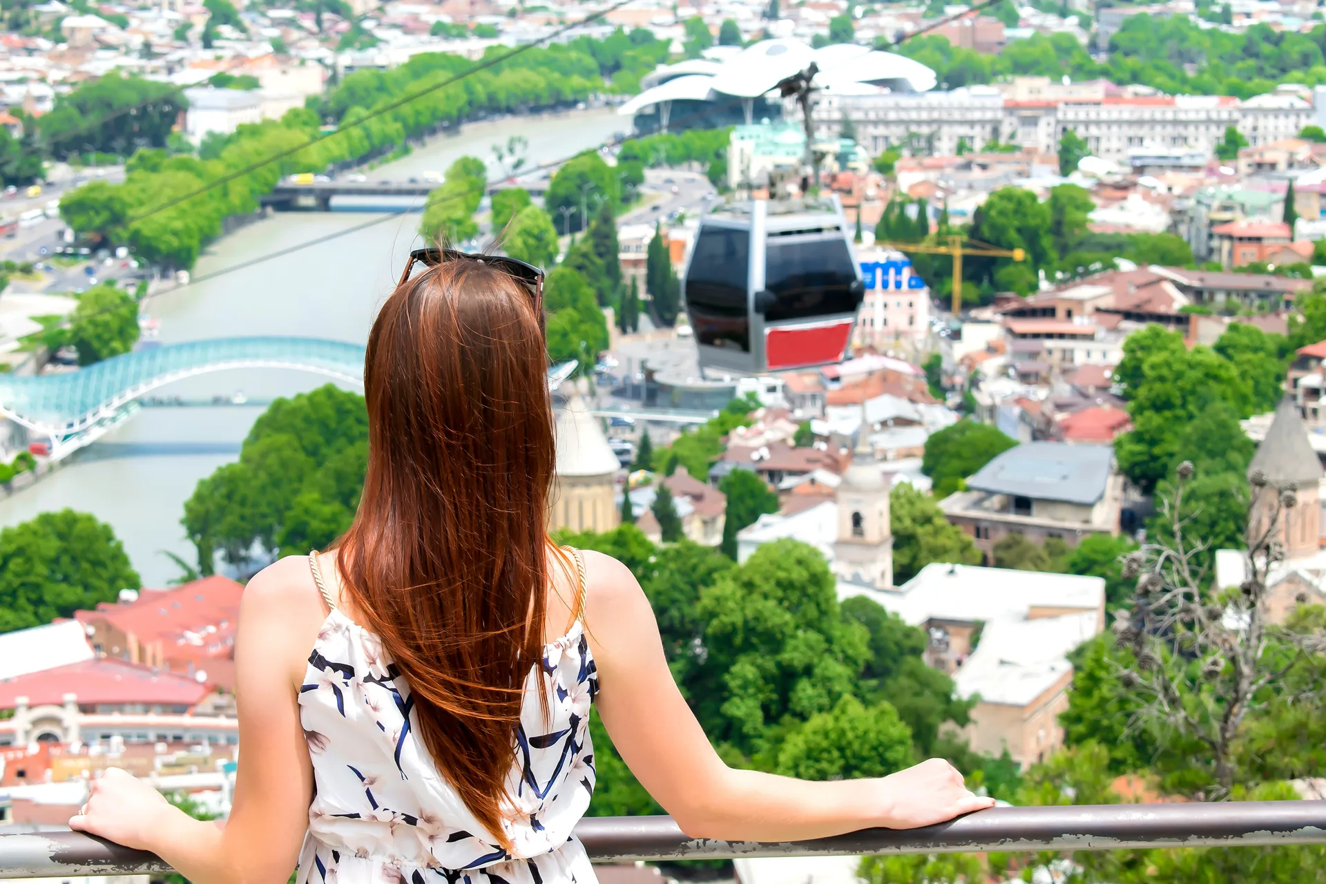 Traveler looking out over Tbilisi panorama with the Bridge of Peace and cable car