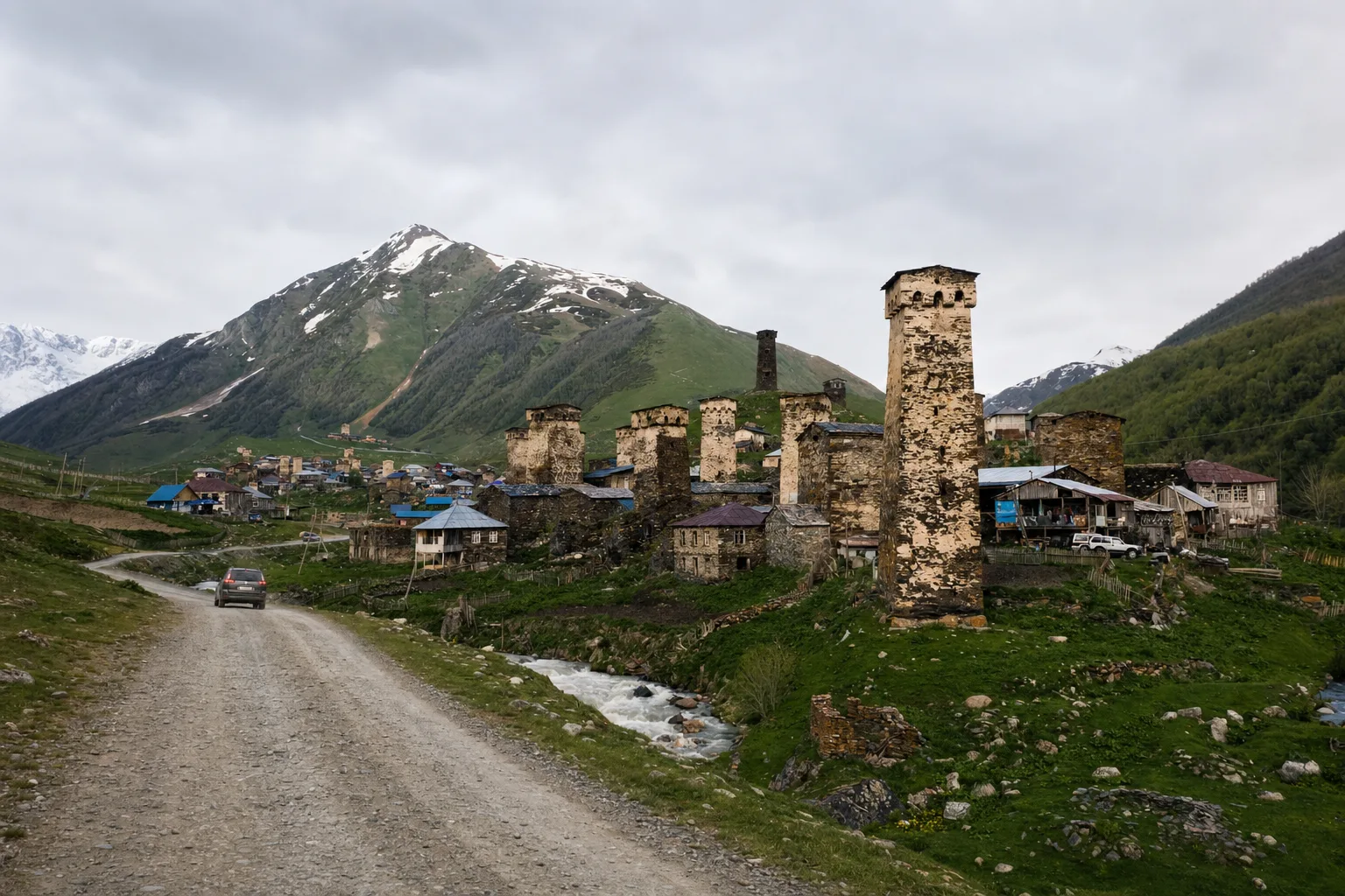 Aerial view of Mestia town in Svaneti with medieval stone towers and snow-capped Caucasus mountains under a blue sky