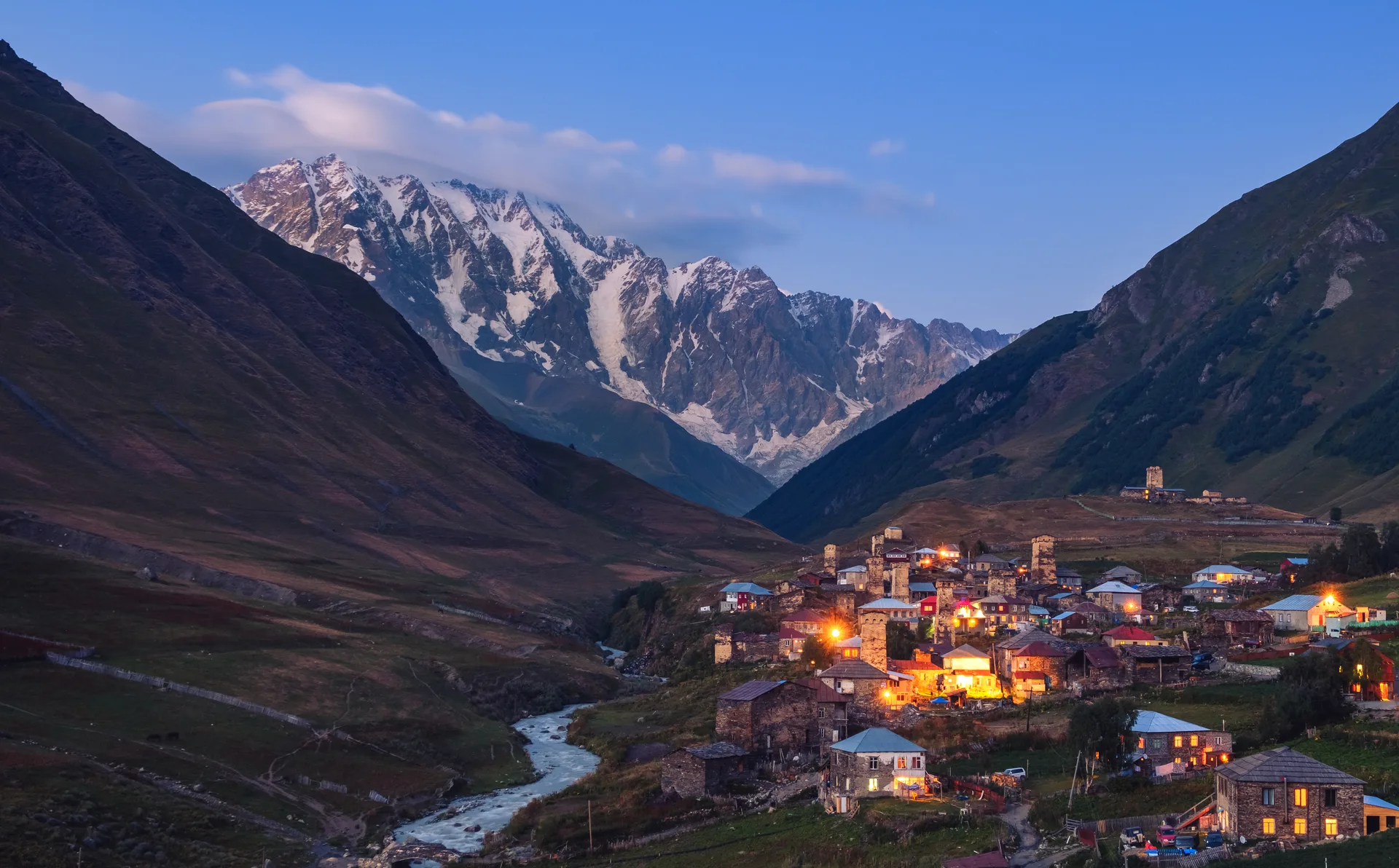 Ushguli village at dusk with ancient stone towers silhouetted against snow-capped mountains in Svaneti