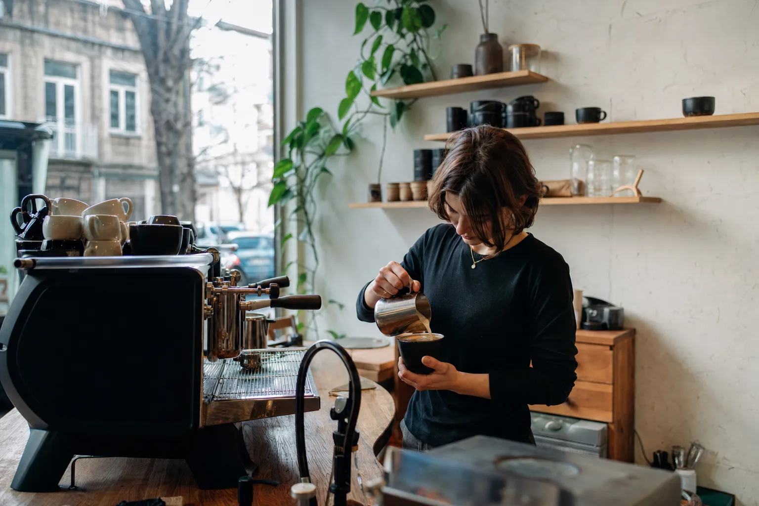 Barista pouring milk into a cup at the wooden counter of a small specialty coffee bar in Tbilisi in mid-morning light