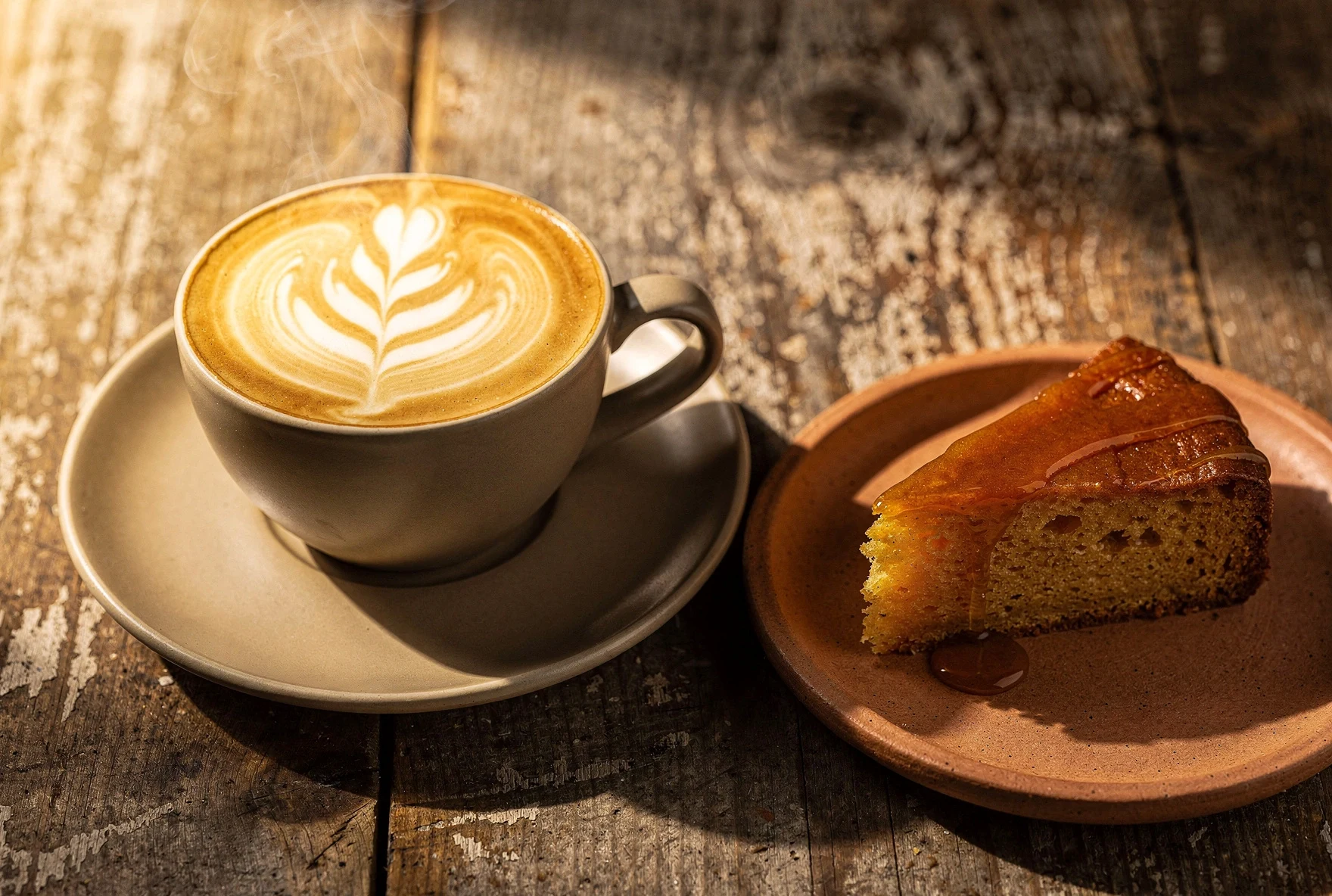 Close-up of a beautifully crafted latte with latte art alongside honey cake on a rustic wooden table