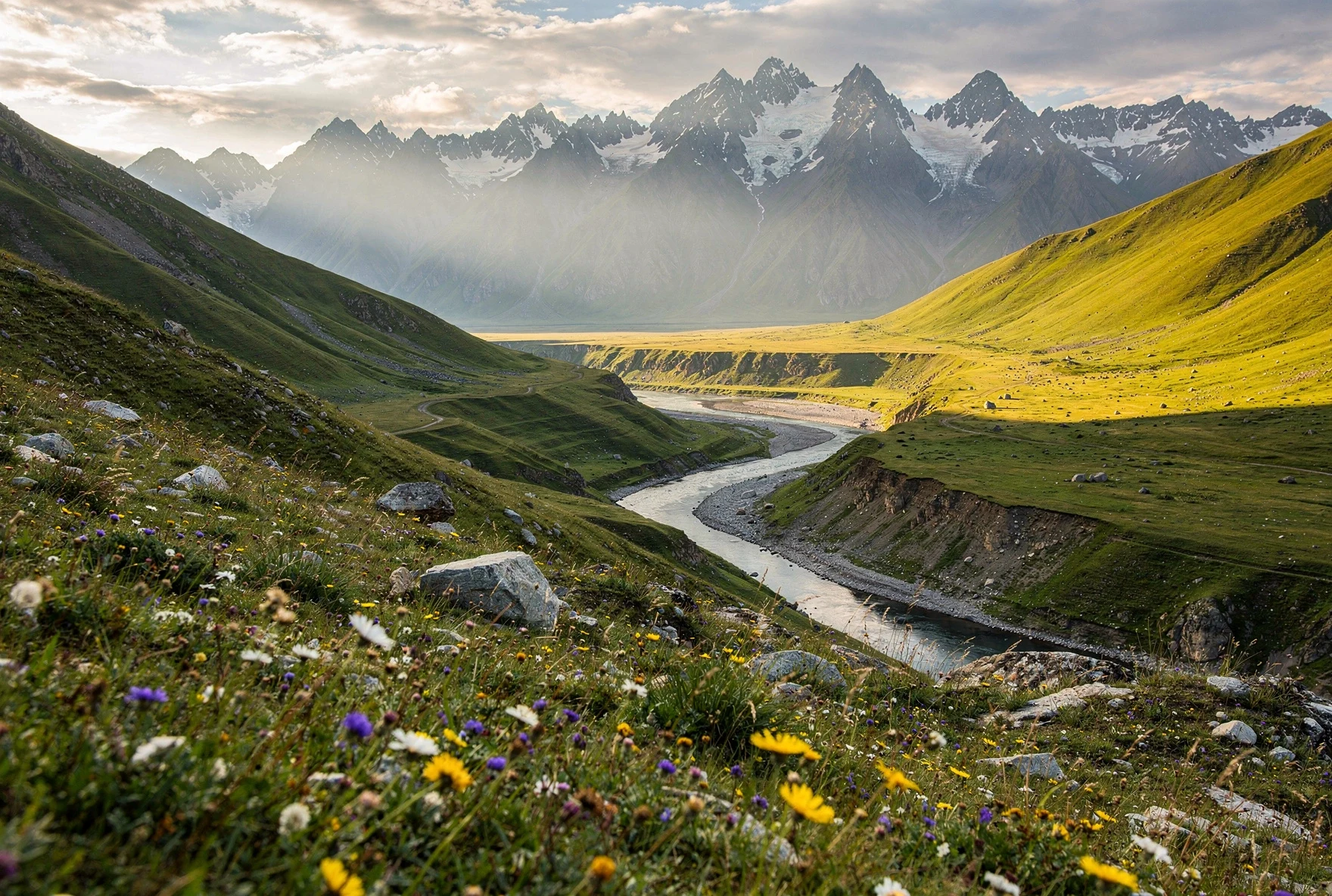 Dramatic Caucasus mountain landscape with green valley, river, and wildflowers