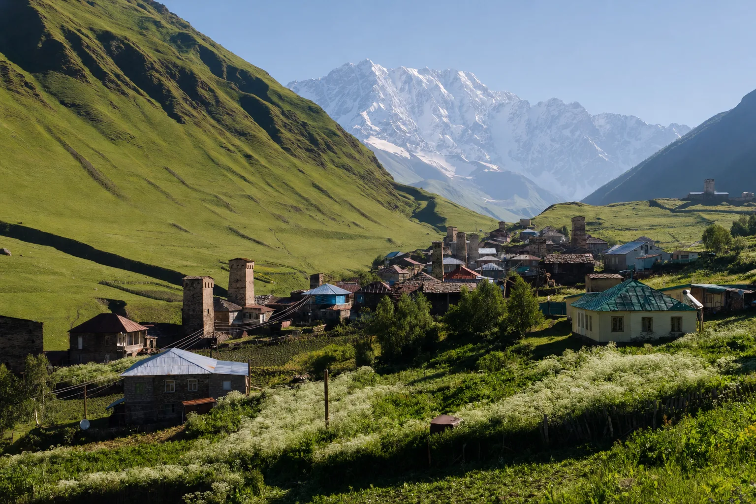 The tower hamlets of Ushguli spread along the upper Enguri valley on a clear morning, with the snow wall of Shkhara closing the view