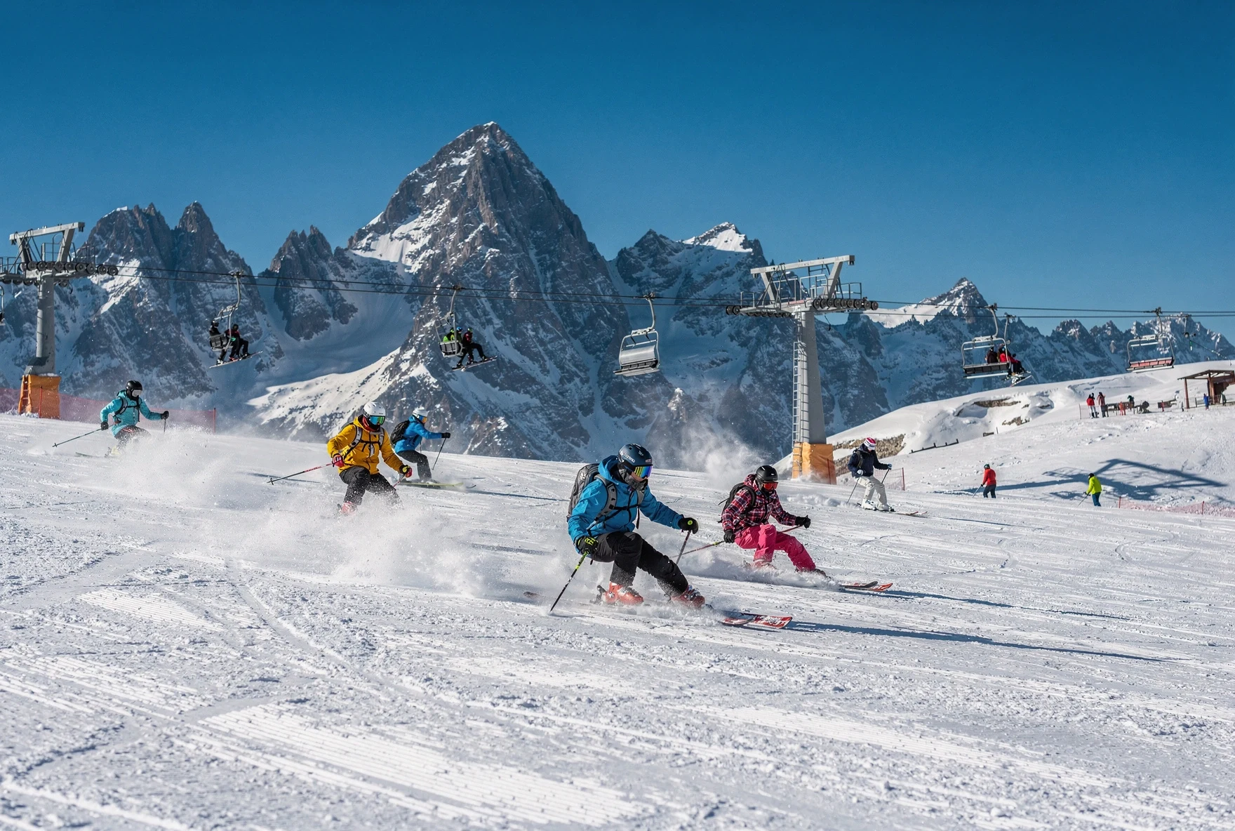 Skiers carving fresh powder on a sunny day at a Georgian ski resort with dramatic Caucasus mountain peaks in the background